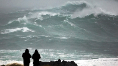 Dúas persoas observan o estado do mar na costa de Valdoviño (EFE/ Kiko Delgado) / Sinal en Directo da cámara web da CRTVG en Muxía